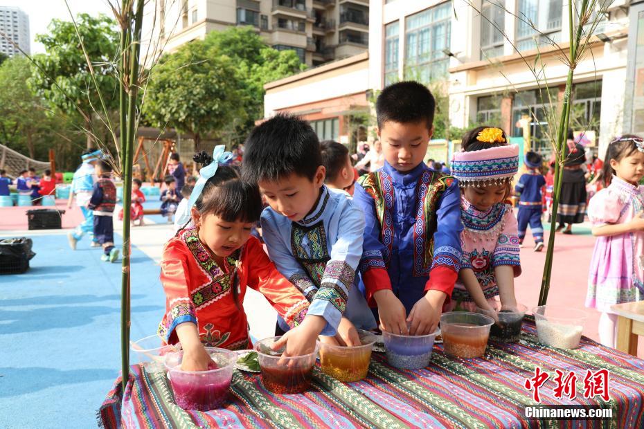 3月27日，在广西南宁市邕宁区一所幼儿园内，师生身着民族服装参加“三月三”民俗活动，通过体验民俗美食一条街、民俗手工一条街的形式，欢度充满童趣与文化气息的“三月三”。图为小朋友在体验制作五色糯米饭。卢虹灵 摄