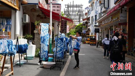 4月14日,贵州省兴义市下纳灰村,手工艺人在晾晒扎染的衣物,游客在村里闲逛。周燕玲 摄 4月14日,贵州省兴义市下纳灰村,手工艺人在晾晒扎染的衣物,游客在村里闲逛。周燕玲 摄