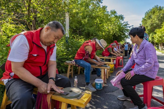 今年7月25日，克拉玛依区昆仑街道南泉社区，“铁老汉磨刀队”成员为居民磨刀。田国建 摄
