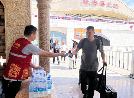 志愿者为到站旅客发放免费矿泉水解暑降温。 胡源 摄