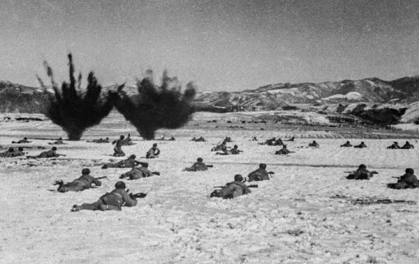 1950年11月， 抗美援朝第二次战役， 东线长津湖战役中，志愿军在敌人埋在阵前的地雷和炮弹的轰击下，在冰天雪地中匍匐前进。图左侧，一战士跃起向30米开外的美军目标投掷手榴弹。 张崇岫 摄