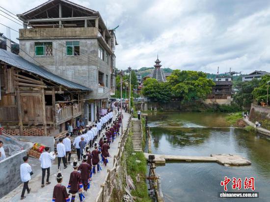 2025年8月7日是贵州省黔东南苗族侗族自治州从江县西山镇顶洞村一年一度新米节，也是当地侗族的成人礼。全村即将迈入成人行列的少男少女，身着节日盛装，欢聚于鼓楼与风雨桥之间，吟唱着悠扬的侗歌，向先祖虔诚地宣告自己的成年，期盼着在爱情的田野上自由驰骋，在事业的征途上勇敢前行，祈福得到先祖的保佑。图为顶洞村的侗族少男少女前往鼓楼准备参加成人礼。（无人机照片）吴德军 摄