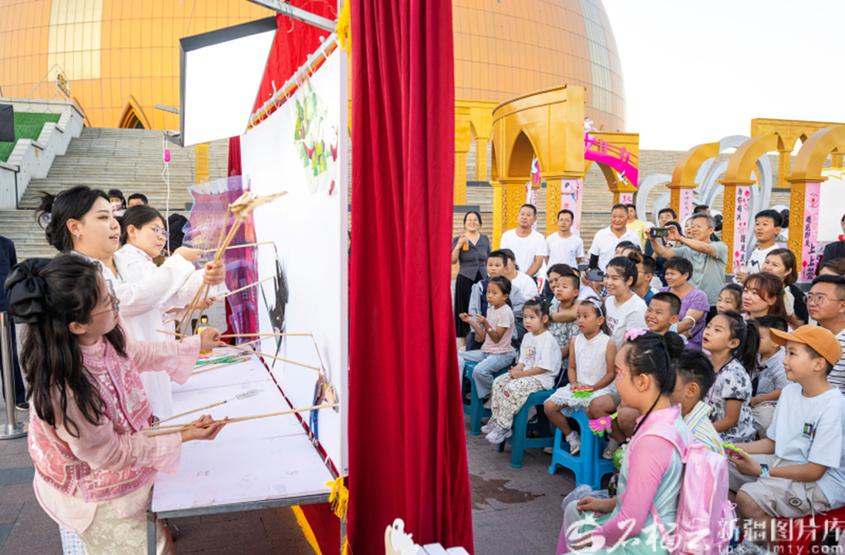 8月29日，新疆大剧院广场，市民在观看皮影戏演出。何龙摄

