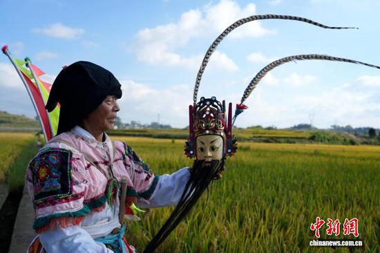 图为9月24日，叶守兴在西秀区旧州镇的稻田间查看地戏面具。石小杰 摄