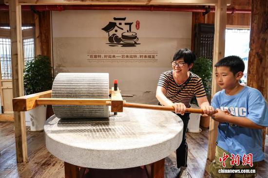 10月4日，游客在乌江寨体验推石磨。中新社记者 瞿宏伦 摄
