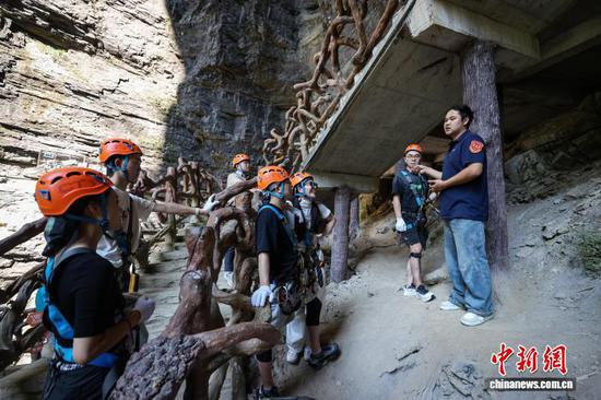 10月11日，贵州省遵义市绥阳县双河洞景区安全员在给游客讲解“悬崖之上·侠客咖啡”项目注意事项。该景区推出的“悬崖之上·侠客咖啡”成为打卡新热点，该项目以“极限挑战喝咖啡”为特色，体验者完成钢索平衡挑战和飞拉达攀岩后即可兑换咖啡，吸引众多游客挑战。中新社记者 瞿宏伦 摄