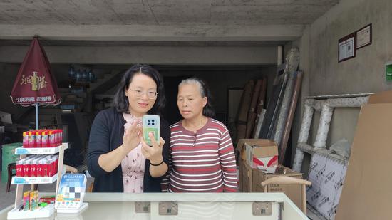 图为普法人员向上门指导老年零售户安装“反诈APP”。杨克 摄 图为普法人员向上门指导老年零售户安装“反诈APP”。杨克 摄