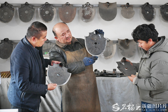 12月2日，艾买提·亚森（中）在阔克旗手工艺专业合作社产品展示区，为顾客介绍传统手工制作的坎土曼。