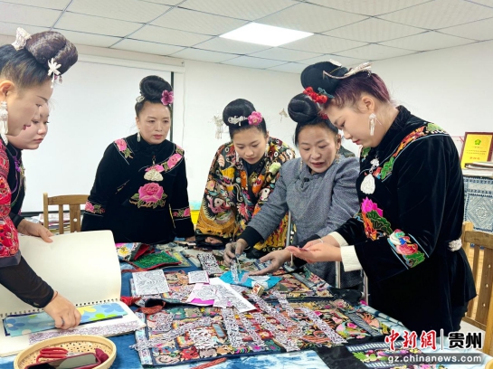 图为张艳梅和绣娘们在讨论2026年的新品设计。