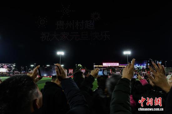 1月1日晚，贵州省黔东南苗族侗族自治州榕江县元旦专场无人机编队表演、烟花秀在“村超”球场上演。图为民众在拍摄无人机编队呈现的“贵州村超，祝大家元旦快乐”。