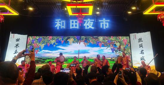 游客在和田夜市品尝特色美食的同时观看精彩歌舞表演。（资料图）