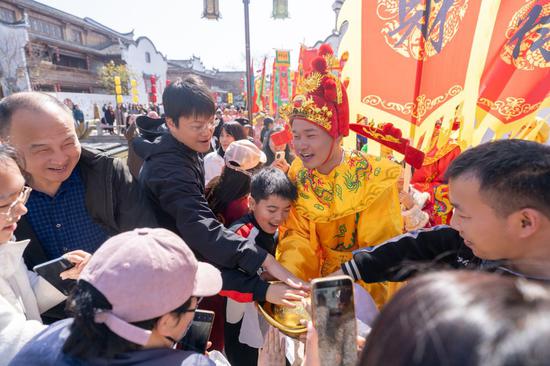 图为浙江省义乌市佛堂古镇上“迎财神”活动，游客与“财神”热情互动。（受访者供图）