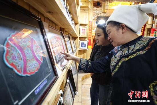 3月1日，韦桃花（右）在展厅给游客介绍马尾绣作品。水族马尾绣是贵州省黔南州三都水族自治县水族妇女世代传承的一种特殊刺绣技艺，被称为中国刺绣的“活化石”。马尾绣以丝线缠裹马尾并盘在描绘好的花纹轮廓上，再根据轮廓线绣出各种图案，工艺独特、复杂。62岁的韦桃花从小学习马尾绣制作技艺，是中国国家级非物质文化遗产水族马尾绣代表性传承人。50多年来，韦桃花在研究和继承传统马尾绣制作方法的基础上大胆创新，在图案设计、刺绣等工艺方面形成自己独有的制作风格，创作出一批精美独特的马尾绣作品深受消费者喜爱。中新社记者 瞿宏伦 摄