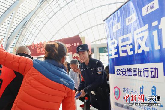 图为北京铁路公安局天津公安处天津西站派出所实习民警祁业美正在向旅客发放反诈宣传单，并热情与旅客交流。（北京铁路公安局天津公安处供图）
