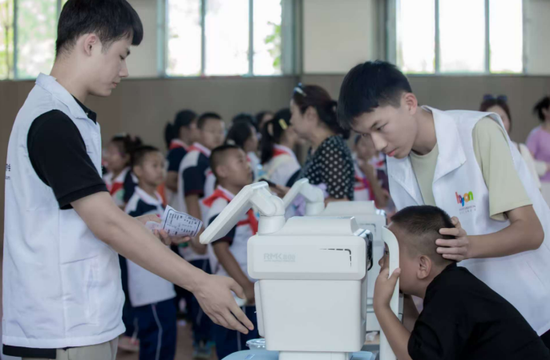 在第十一季“爱目行动”新疆石河子站活动现场，工行志愿者为小学生进行视力筛查（2025年6月18日摄）。e