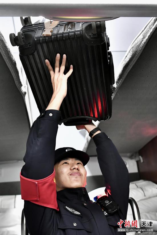 图为动集列车车厢内，乘警俯身帮旅客加固行李架上的行李箱，细致排查隐患，保障旅途安全。（北京铁路公安局天津公安处供图）