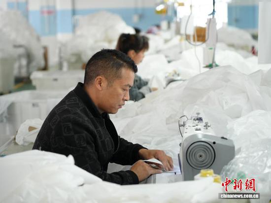 图为3月31日，工人在生产线上用缝纫机缝制车衣。石小杰 摄