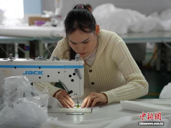 图为3月31日，工人在生产线上用缝纫机缝制车衣。石小杰 摄