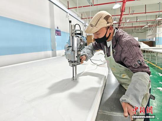 图为3月31日，裁剪工在生产车间里用电推刀裁布。石小杰 摄