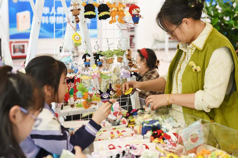 色彩繽紛的鉤織手作攤位吸引了市民駐足，大家認(rèn)真挑選可愛的手工掛件。克拉瑪依融媒記者 王兆國 攝