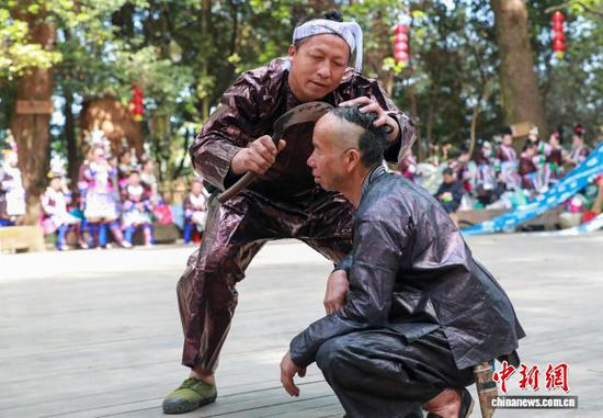 图为苗族群众在岜沙苗寨向游客表演镰刀剃头。罗京来 摄
