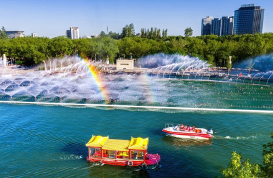 5月6日傍晚，克拉玛依河中心景区，画舫与快艇载着游客在河面畅游，音乐喷泉在阳光照耀下折射出绚丽彩虹。经过试运行，自 5月起，景区画舫、快艇正式开航，游客可乘船一览克拉玛依河两岸夏日风光。同时，九龙潭景区的碰碰船、鸭子船也已陆续下水，迎接八方来客。（闵勇）5
