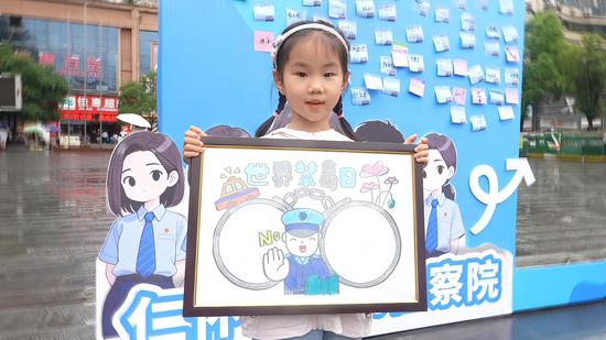 禁毒游园会现场，小朋友展示自己的禁毒画作。