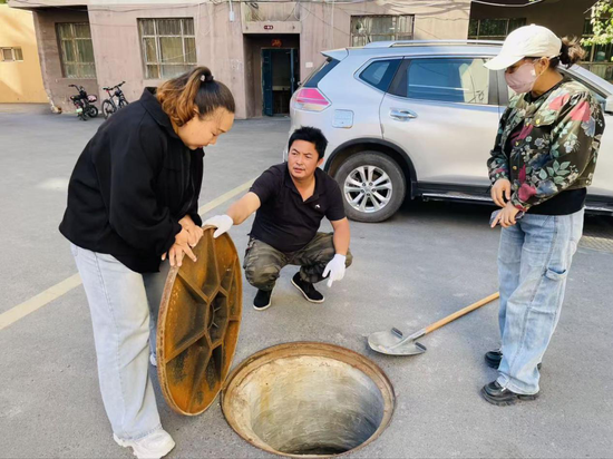 社区干部和维修人员一起查看下水管道疏通情况。