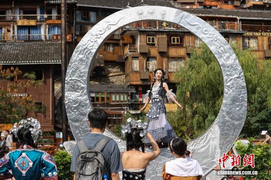 西江千户苗寨，游客身着民族服饰，以吊脚楼群为背景拍照留念。中新社记者 瞿宏伦 摄