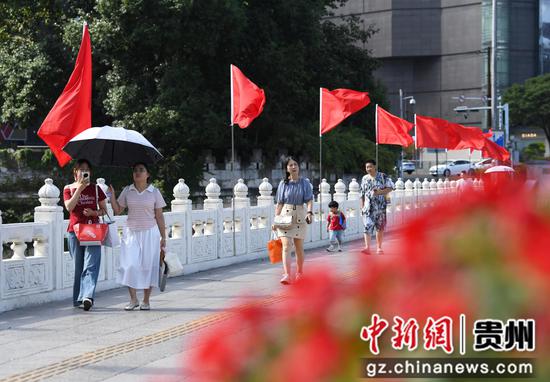 9月24日，在贵阳市南明区南明桥上，市民游客在迎风招展的红旗下。
