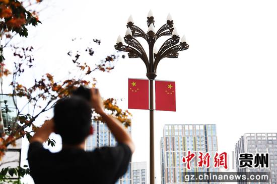 9月24日，在贵阳市南明区花果园大街，一位摄影爱好者正在用相机拍摄灯杆道旗。