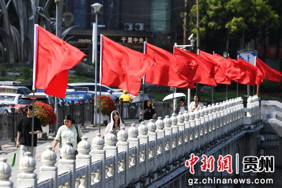 9月24日，在贵阳市南明区南明桥上，市民游客在迎风招展的红旗下穿行。