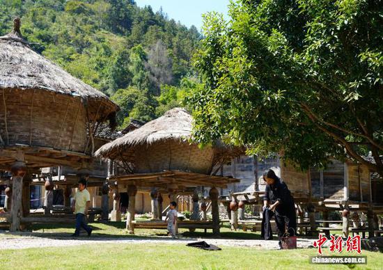 10月10日，贵州省荔波县瑶山古寨，白裤瑶族人在禾仓群旁行走和晒布。中新社记者 周燕玲 摄