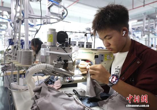图为10月14日，贵州省都匀市绿茵湖轻纺产业园内，戴着耳机、电子手表的年轻人在车间里工作。中新社记者 泱波 摄