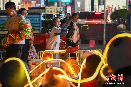图为10月14日，贵州都匀街头夜市，一名女孩抬手抛出套圈，享受夜间闲适时光。中新社记者 李嘉娴 摄