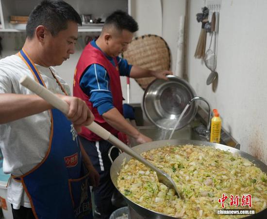 图为10月27日熊泽珲在“爱心厨房”里炒白菜、翟饶在清洗菜盆。中新社记者 周燕玲 摄