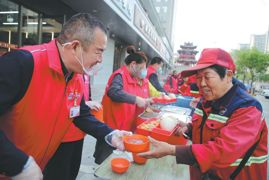 Zhang Changqin (left) hands a bowl of porridge to a sanitation worker in Yuncheng, Shanxi province, on April 15. HU ZENGCHUN/FOR CHINA DAILY