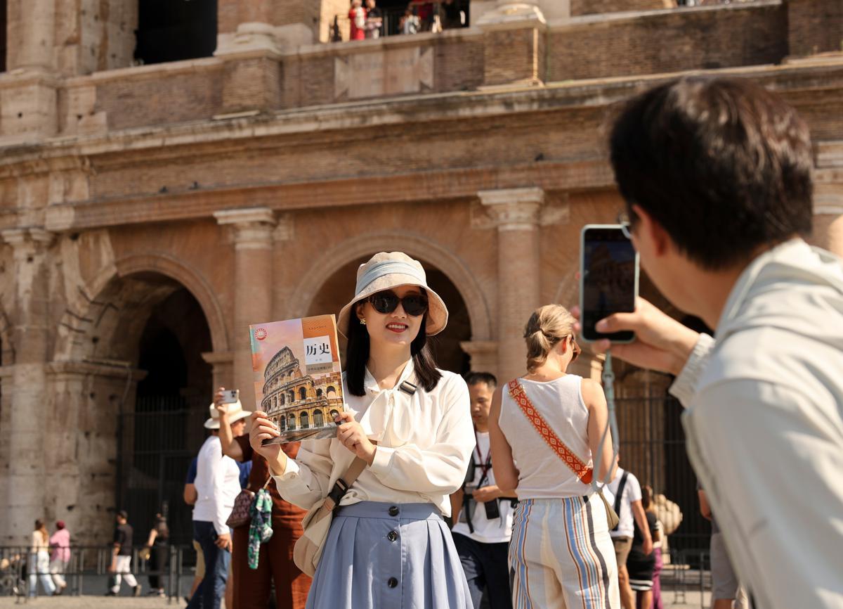 A Chinese tourist poses for a photo on Sunday outside the Colosseum in Rome, Italy, while holding a Chinese senior high school history textbook, the cover of which features the historical structure. Rome received a large number of Chinese tourists during the recent National Day holiday. LI JING / XINHUA