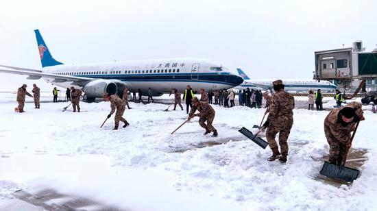 Officers of the People's Armed Police Force and staff workers clear snow from the tarmac at Wuhan Tianhe International Airport in Hubei province on Sunday. As of noon on Sunday, 315 flights had been canceled. (Photo by CHEN XIAODONG / FOR CHINA DAILY)