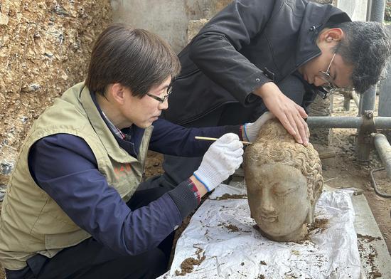 Archaeologists clean a stone Buddha head that was discovered at the Leigutai caves of the Longmen Grottoes in Luoyang, Henan province, in November. (Photo provided to China Daily)