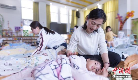 Teachers comfort toddlers before their afternoon nap at a kindergarten in Cuihu Jiayuan residential community in Donggang District of Rizhao, east China’s Shandong Province, April 18. (Photo: China News Service/Yin Zhaogong)