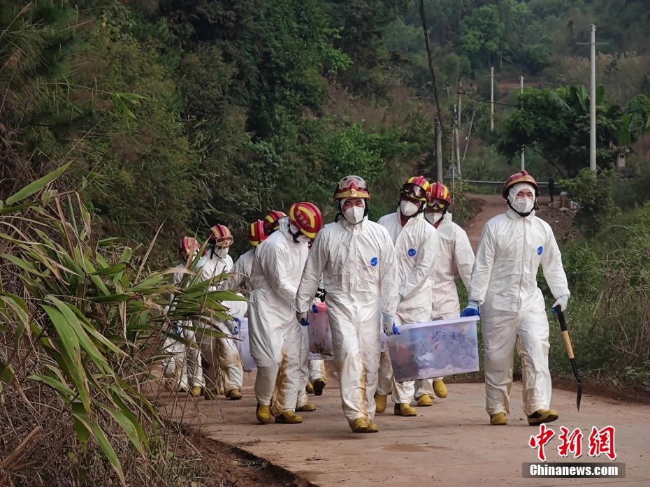 3月25日,救援人员用塑料箱带着乘客衣物走出东航飞行事故搜救现场.