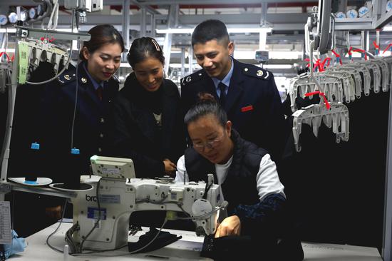 国家税务总局黔西市税务局关注当地出口退税企业发展，为相关企业提供“一企一策”个性化税费服务，辅导企业依法依规适用税费政策，更好地防范跨境经营税收风险。图为税务人员在贵州质品服饰有限公司了解生产工艺。刘一帆摄